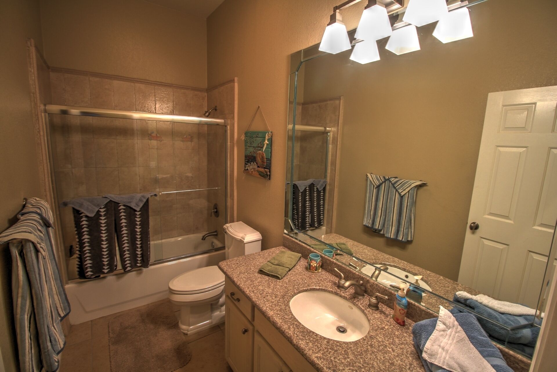 A bathroom with a shower, toilet, sink, and a large mirror.