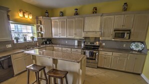 A kitchen with a central island, two stools, stainless steel appliances, and light-colored cabinetry.