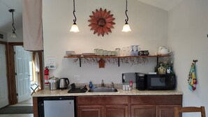 Una cocina con armarios de madera, lavavajillas integrado, microondas y un lavabo. Hay una repisa sobre el lavabo con diferentes vasos y un objeto decorativo.