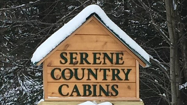 Una señal de madera para Serene Country Cabins con un adorno de coronas nevadas.