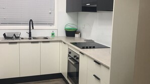 A kitchen with white cabinets, a black countertop, and a window with blinds.