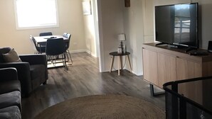 A living room with a ceiling fan, a TV on a wooden cabinet, a round woven rug, and a dining area with a table and chairs.
