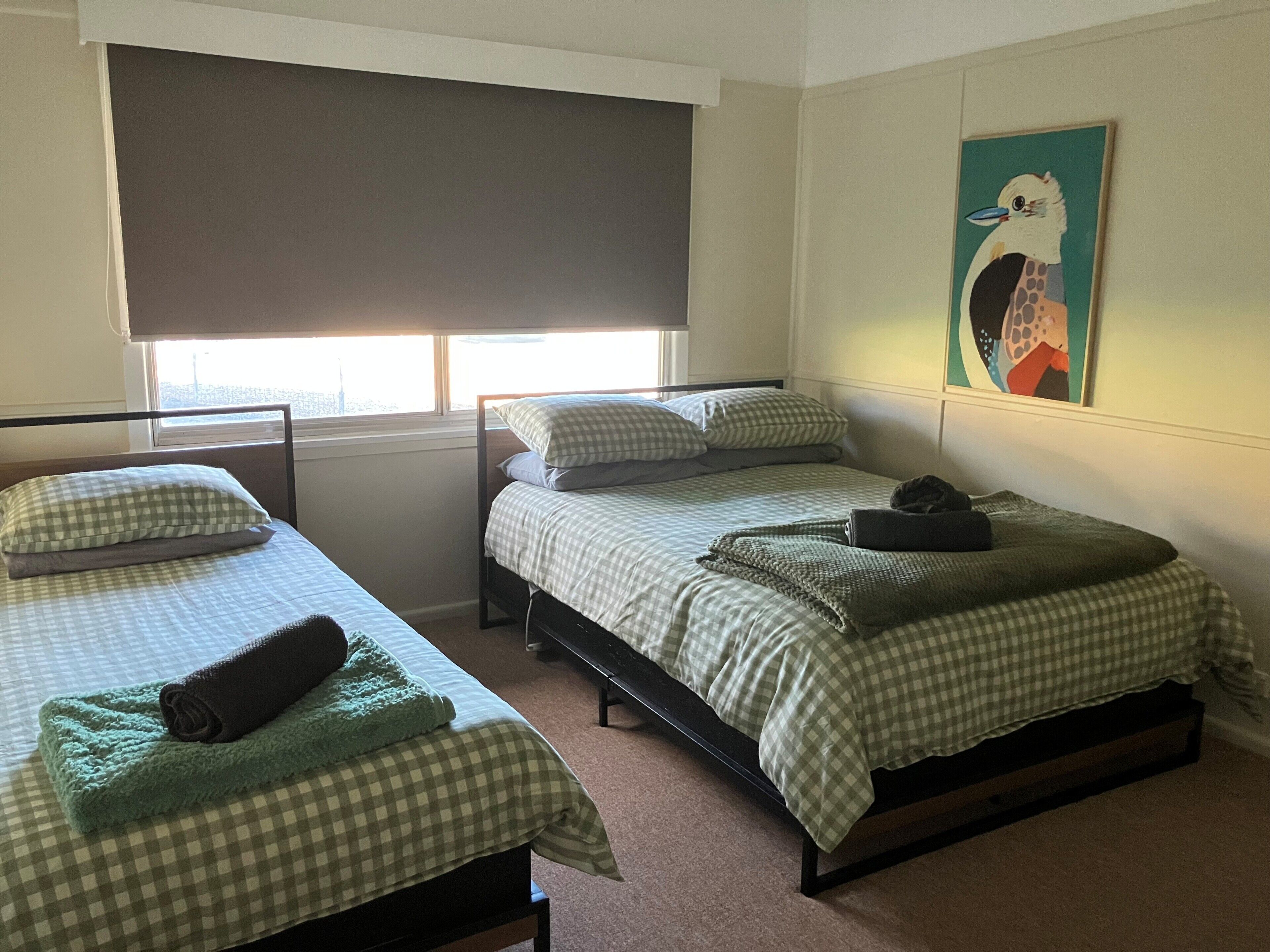 Ein Zimmer mit zwei Einzelbetten, einem Fenster mit Jalousie, einem Bild an der Wand und einem Teppichboden.