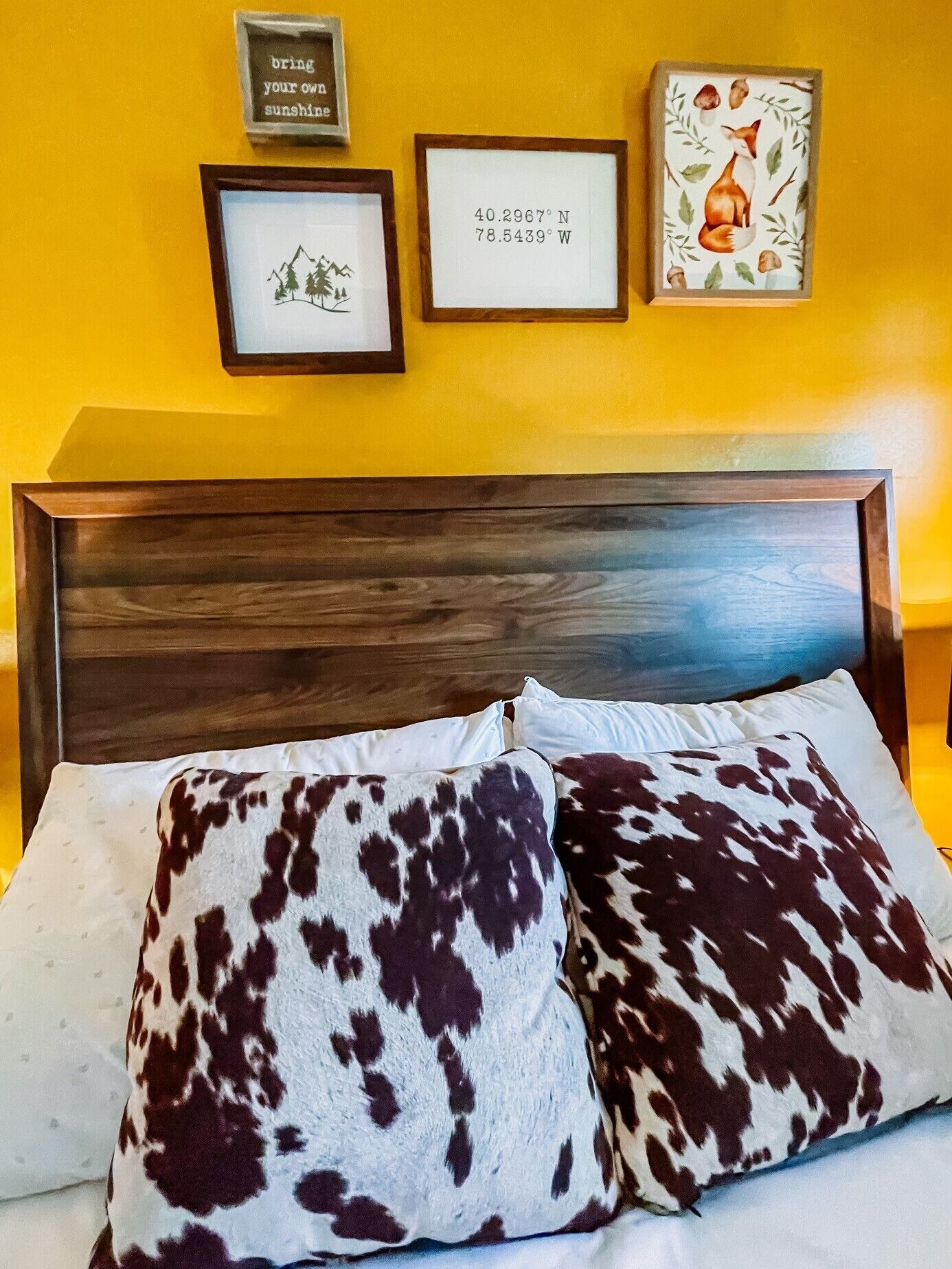 Ein Bett mit zwei gemusterten Kissen, einem Holzkopfbrett und drei gerahmten Bildern an der Wand.