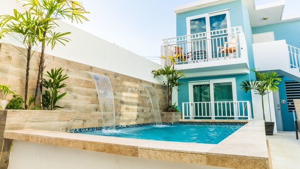 Un bâtiment moderne à deux étages doté d’une piscine, d’une cascade et d’un balcon aménagé avec du mobilier d’extérieur.