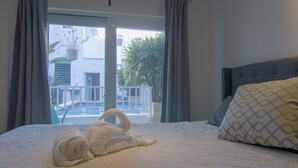 Une chambre d’hôtel avec un lit, une vue sur une piscine et sur la verdure environnante, et un balcon doté d’une balustrade.