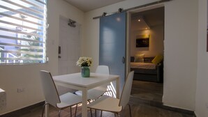 Une pièce avec une table et des chaises blanches, une porte coulissante bleue et un lit avec des oreillers.