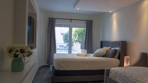 Une chambre à coucher avec un lit, une table de chevet ornée d’un vase de fleurs, une fenêtre avec des rideaux et une vue sur l’extérieur.