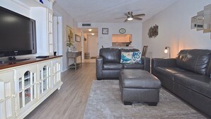 Una sala de estar con un televisor de pantalla plana, sofás de cuero, una mesa de centro y un área de comedor al fondo.