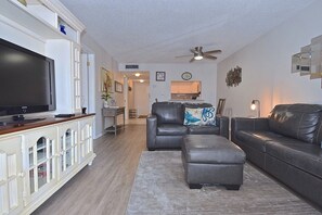 A living room with a flat-screen TV, leather sofas, a coffee table, and a dining area in the background.