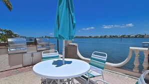 Un patio al aire libre con una parrilla, una mesa y sillas, con vista a una masa de agua.