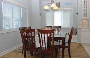 A dining area with a wooden table and chairs, a bench, and a window with blinds. - Patient Tide Beautiful 3 BR Ocean View Home; Community Pool & Tennis Courts (North Topsail Beach)