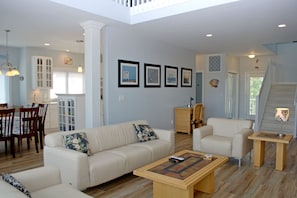 A spacious living area with a high ceiling, a dining area with wooden chairs, a sofa set, and a coffee table.