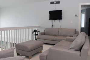 A living room with a grey sofa, a matching ottoman, and a mounted flat-screen TV.