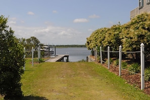A grassy pathway leading to a dock by a body of water, with a fence and trees on the right. - Patient Tide Beautiful 3 BR Ocean View Home; Community Pool & Tennis Courts (North Topsail Beach)