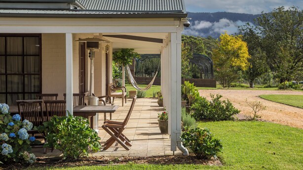Un patio cubierto con mobiliario exterior, una hamaca y vistas a un paisaje montañoso.