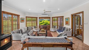 Amplia sala de estar con chimenea, asientos cómodos, un televisor grande y vistas panorámicas por las ventanas.