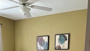 Ein Schlafzimmer mit einem Bett, einem Nachttisch, einer Lampe und einem Deckenventilator.