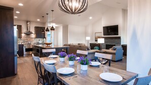 A modern kitchen with a central island, dining area with chairs and a table set for four, and a living area with a sofa and a TV. - Friendcation in Bend ~ hot tub ~ bunk beds ~ resort pool + amenities ~ golf ~🐶 (Bend)