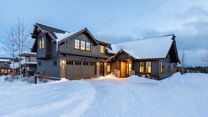 A large, multi-story house with a snow-covered driveway and a well-lit entrance. - Friendcation in Bend ~ hot tub ~ bunk beds ~ resort pool + amenities ~ golf ~🐶 (Bend)