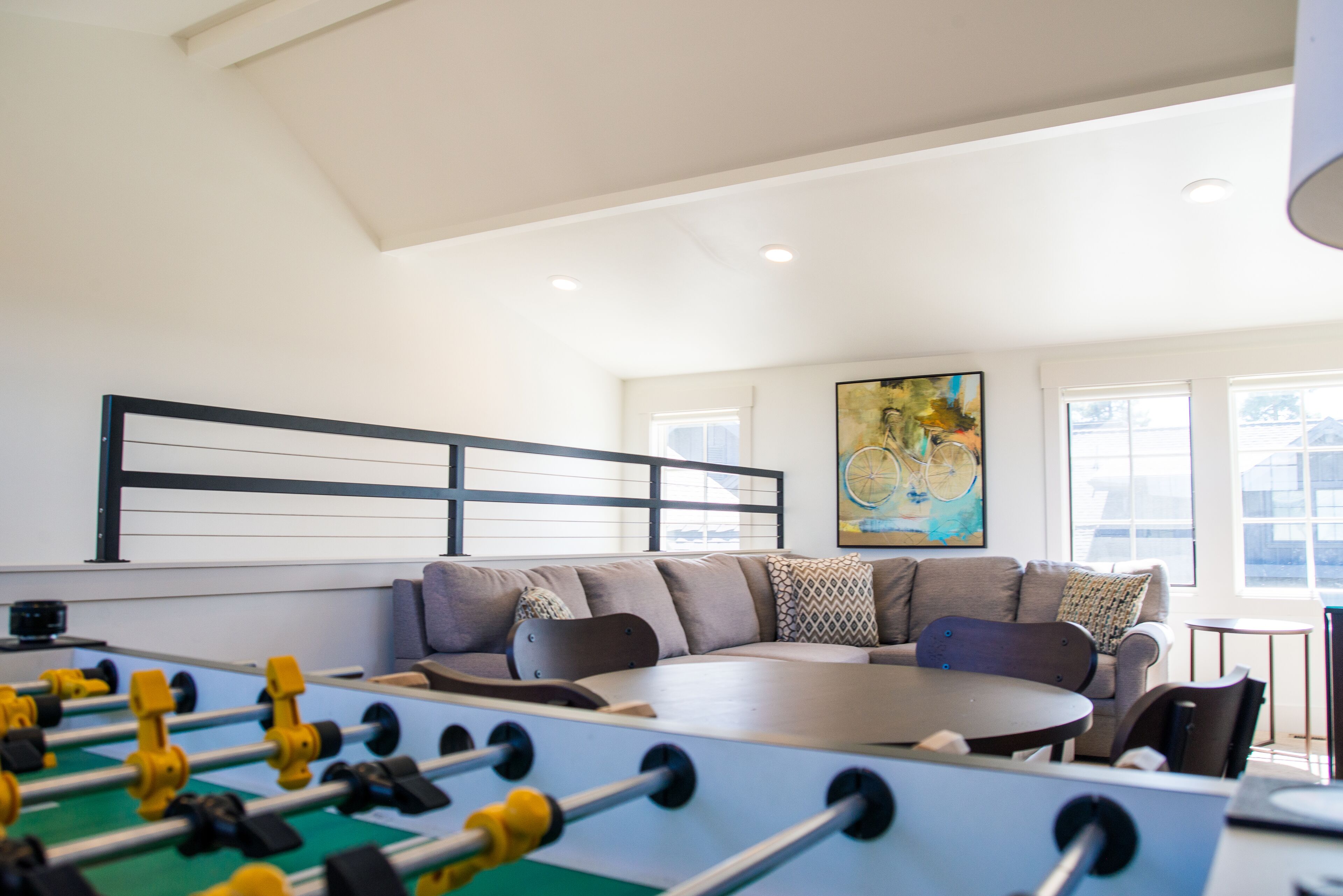 Una sala de estar moderna con una mesa de futbolín, una mesa de centro redonda y un sofá con cojines estampados.