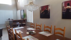 Uma sala de jantar com mesa de madeira, cadeiras, um candelabro e obras de arte nas paredes.