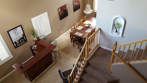 Uma sala de jantar com mesa e cadeiras de madeira, uma área de bar com balcão e uma escada com corrimão de madeira.