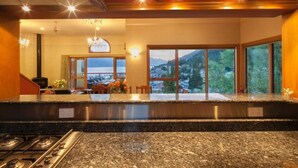 A modern kitchen with granite countertops, stainless steel appliances, and large windows offering a view of a mountainous landscape. - Expansive home in the Heart of Queenstown with Stunning Views. (Queenstown Hill)