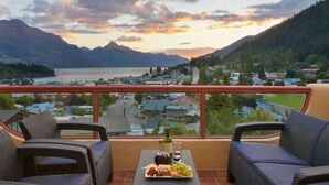 A balcony with wicker furniture, a bottle of wine, and a plate of snacks. - Expansive home in the Heart of Queenstown with Stunning Views. (Queenstown Hill)