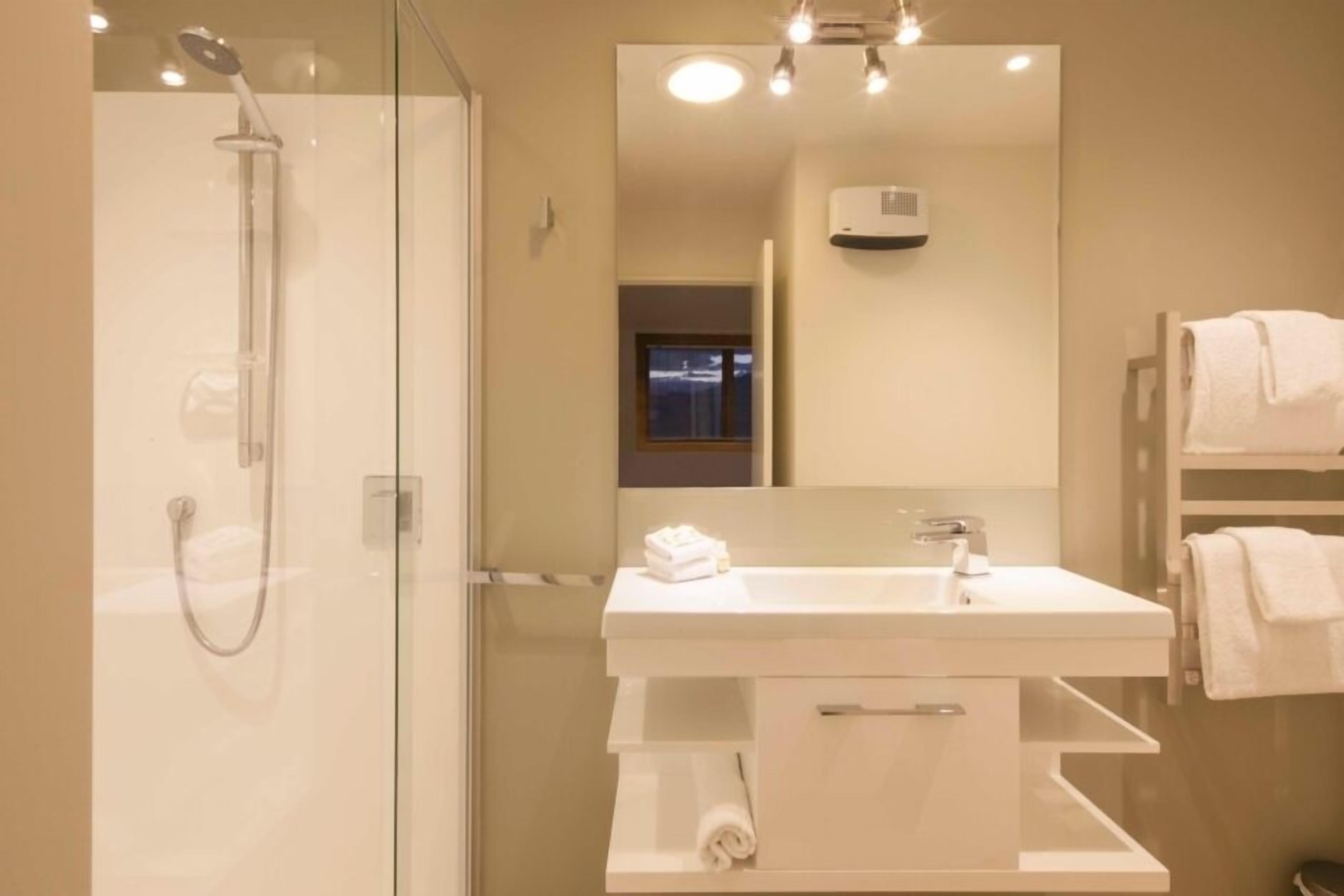 A modern bathroom with a glass-enclosed shower, a white sink with a mirror above it, and a towel rack with towels.
