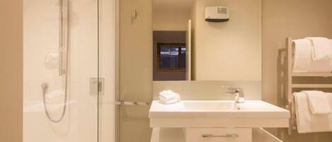 A modern bathroom with a glass-enclosed shower, a white sink with a mirror above it, and a towel rack with towels.