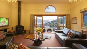 A spacious living room with a fireplace, leather sofas, a coffee table with a vase of flowers, and a large window offering a scenic view. - Expansive home in the Heart of Queenstown with Stunning Views. (Queenstown Hill)