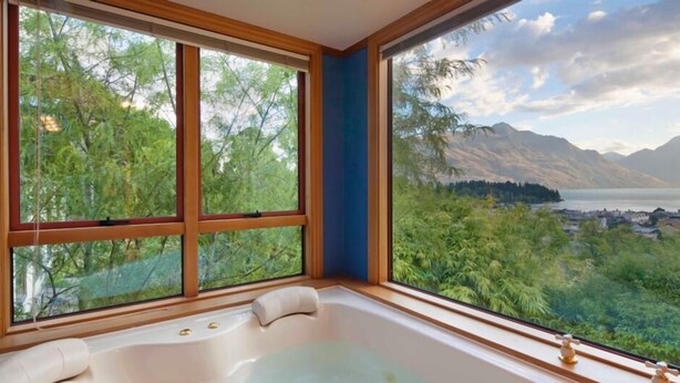 A room with a large window, a bathtub, and a view of mountains and trees. - Expansive home in the Heart of Queenstown with Stunning Views. (Queenstown Hill)