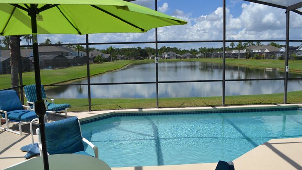 A pool area with a view of a lake, surrounded by houses, and equipped with lounge chairs and an umbrella.