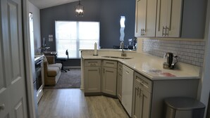 A modern kitchen with light wood flooring, beige cabinetry, and a stainless steel sink.