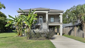 A two-story house with a front porch, a covered entryway, and a small front yard with a banana tree and flowering plants. - View the Beach from your porch.  
Best location, 5 blocks to downtown  (Biloxi)