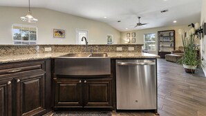 A kitchen with dark wood cabinets, a stainless steel sink, and a dishwasher. There is a ceiling fan, recessed lighting, and a window with blinds. - View the Beach from your porch.  
Best location, 5 blocks to downtown  (Biloxi)