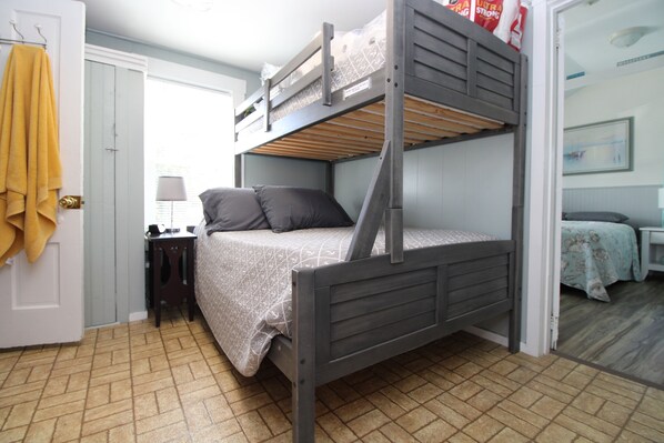 A bunk bed with a desk and chair, a lamp, and a bed with a patterned bedspread.