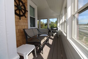 A covered porch with a wooden wall, a white table, two chairs, and a view of the outdoors.