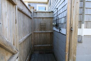 Un espace de douche extérieur en bois, doté d’un pommeau de douche en métal et d’une porte en bois.