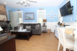 Un salon avec un canapé, une table basse et un téléviseur. On y trouve une cheminée et un mur orné d’une enseigne indiquant « Plage ».
