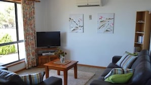 Ein Wohnzimmer mit einer Couch, einem Couchtisch mit einer Vase, einem Flachbildfernseher und Kunstwerken an der Wand.