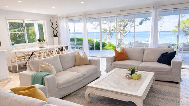 Un salón amplio con dos sofás, una mesa de centro y ventanas grandes que ofrecen vista al mar.