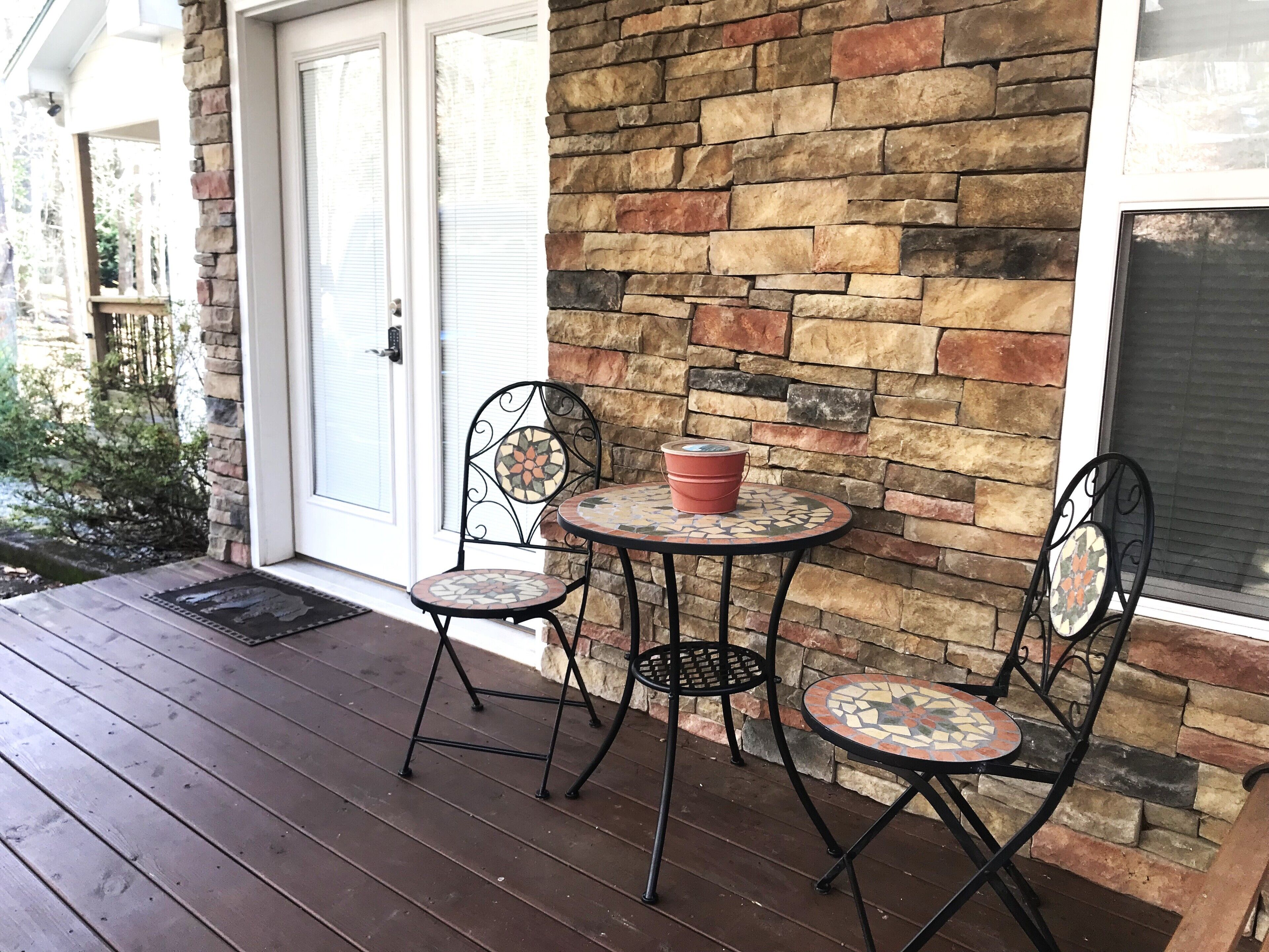 A covered outdoor area with a stone wall, two metal chairs, and a small round table with a red bucket.