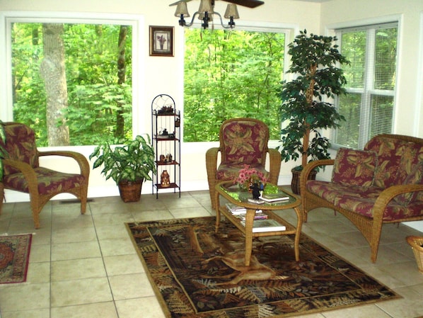 Un salon lumineux, baigné de soleil, avec une grande fenêtre, une plante en pot, une table basse et un canapé.