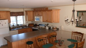 Una cocina con armarios de madera, una isla central y una zona de comedor con sillas y una mesa.