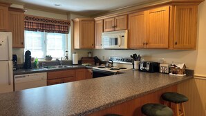 Una cocina con armarios de madera, encimera de granito, microondas, estufa y taburetes de bar.