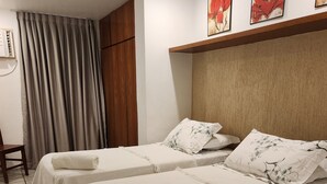 A hotel room with two beds, each with a white bedspread and matching pillows. There is a wooden headboard, a window with curtains, and artwork on the wall.