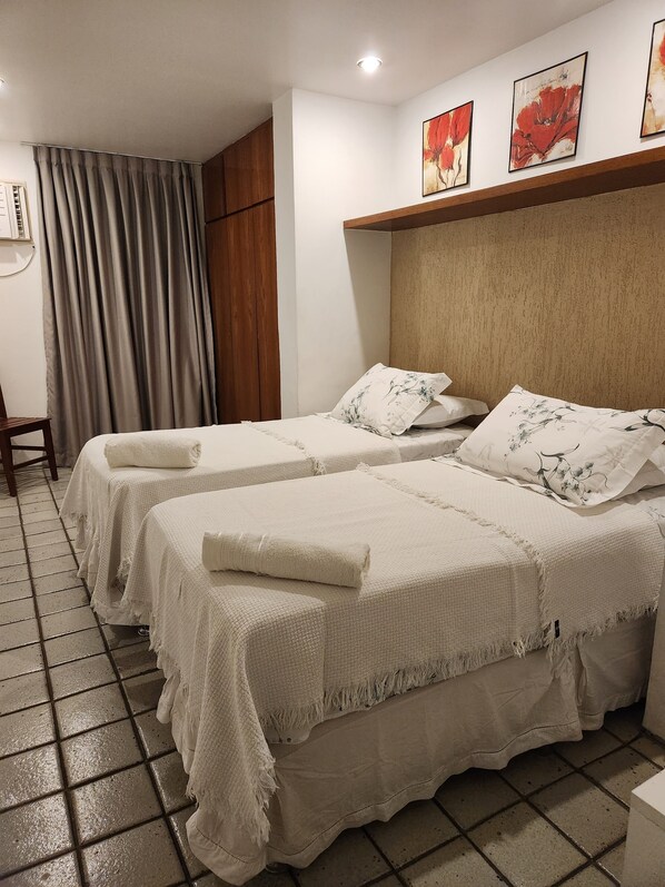 A hotel room with two beds, each with a white bedspread and matching pillows. There is a wooden headboard, a window with curtains, and artwork on the wall. - In front of the sea! Enjoy Rio with Tranquility, Comfort and many Facilities!!! (Rio de Janeiro)
