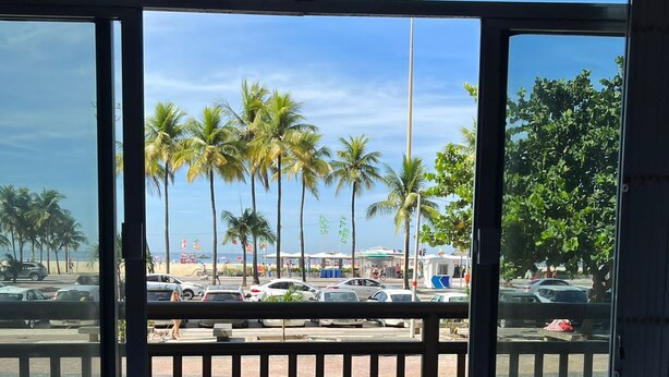A view from inside a building through large windows, overlooking a parking area with several cars and palm trees.